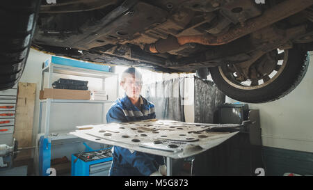 Mechanic at work - automobile's bottom holder under lifted car Stock Photo