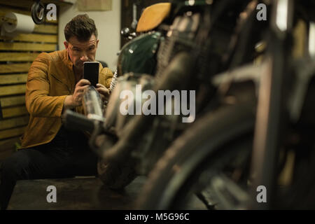 Mechanic taking picture of motorbike with mobile phone Stock Photo