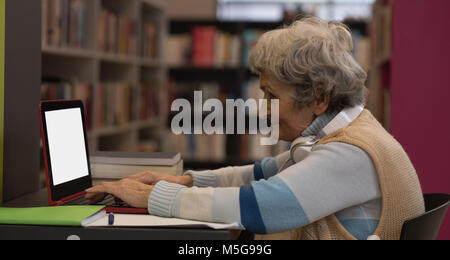 Senior woman using laptop in library Stock Photo