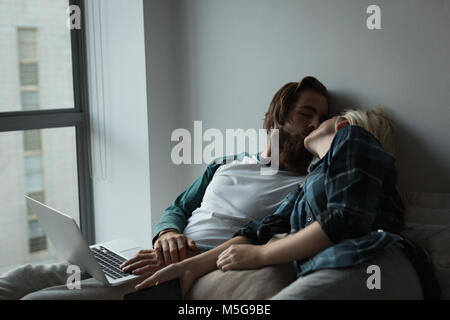 Couple kissing each other while using laptop at home Stock Photo