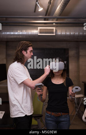 Male executive helping female executive in using virtual reality headset Stock Photo