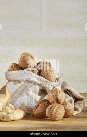 Composition of shelling walnuts in burlap bag on wooden table over the light background, selective focus, close-up. Useful and nutritious snack for ev Stock Photo