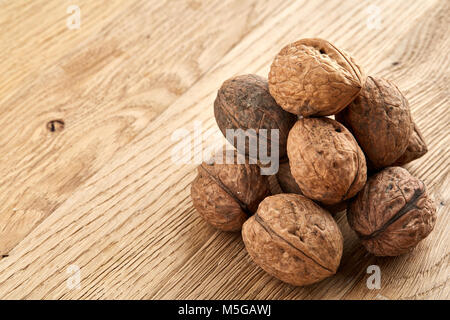 A stack of hard shells of walnuts piled together on light grey fabric cotton napkin and isolated on rustic wooden background, copy space, shallow dept Stock Photo
