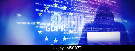 Composite image of hacker wearing black hood while using laptop on table Stock Photo