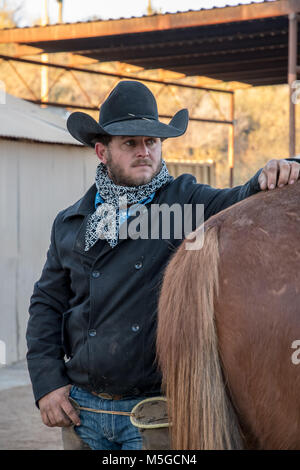 Cowboy in black hat with hand on horse Stock Photo