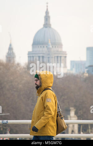 A man wearing a winter coat, crosses Waterloo Bridge, in central London, as freezing air from Russia is to grip the UK in what is set to be the coldest late February in five years. Stock Photo