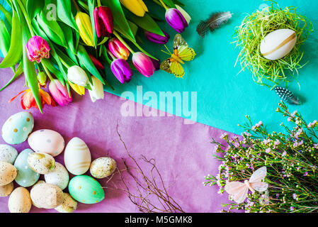 Happy Easter shot from above as flatlay with retro easter eggs, butterfly, easter nest and a bunch of tulips in front of colourful background symboliz Stock Photo