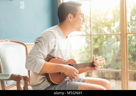 Asian young man hands playing acoustic guitar ukulele at home. Enjoy playing acoustic guitar sunshine in the evening. Stock Photo
