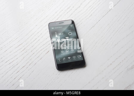 Modern smart phone with home control app on white wooden surface. Stock Photo