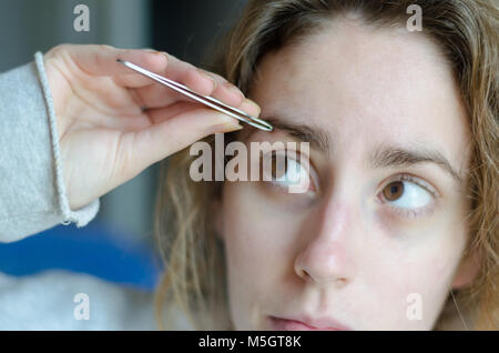 Photograph of a girl plucking her eyebrows with tweezers. Stock Photo