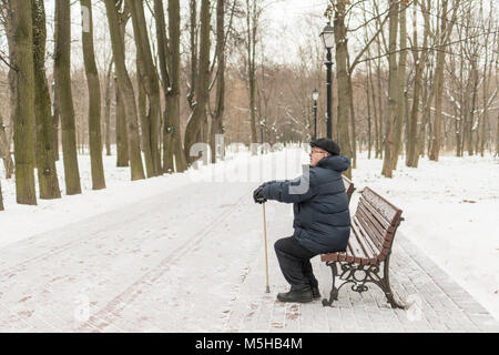 Man - elderly pensioner, sits on a park bench in the winter. High trees, a lantern. Tsaritsyno, Moscow. Stock Photo
