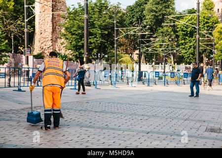 Istanbul, June 15, 2017: Janitor in bright orange uniform sweeping the tile on the street in Sultanahmet district in Istanbul, Turkey. Blue barriers a Stock Photo