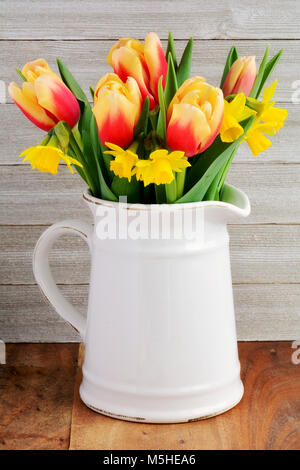 Tulips and daffodils in vintage jub on rustic wooden background.  In vertical format and shot in natural light. Stock Photo