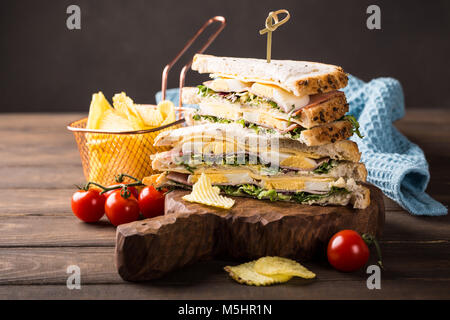 Fresh club sandwich with ham, cheese, boiled eggs and potatoes chips on wooden background. Healthy fast food concept with copy space. Stock Photo