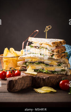 Fresh club sandwich with ham, cheese, boiled eggs and potatoes chips on wooden background. Healthy fast food concept with copy space. Stock Photo