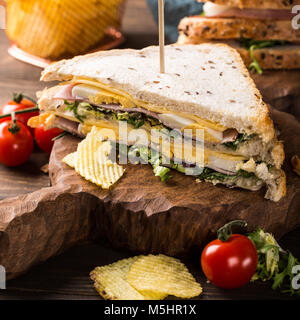 Fresh club sandwich with ham, cheese, boiled eggs and potatoes chips on wooden background. Healthy fast food concept. Stock Photo