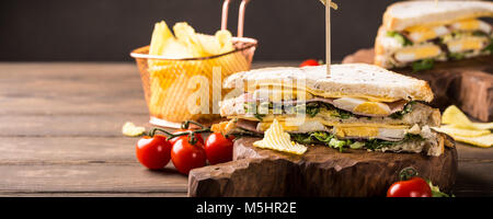 Fresh club sandwich with ham, cheese, boiled eggs and potatoes chips on wooden background. Healthy fast food concept with copy space. Banner. Stock Photo