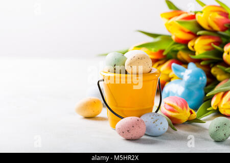 Easter composition with colored quail eggs candies in bucket and spring tulips flowers. Holidays concept with copy space. Stock Photo