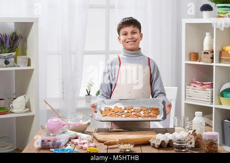 Boy shows a tray of baked cookies in home kitchen interior, homemade food concept Stock Photo