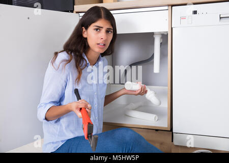Young Woman Holding Sink Pipe And Monkey Wrench In Kitchen Stock Photo