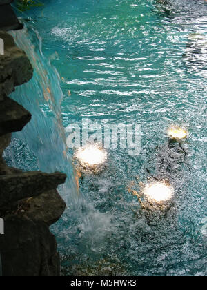 Artificial waterfall pouring into pool with electric underwater lights Stock Photo