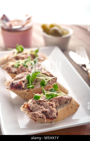 Chicken liver Pate spread on bread slices with greens and condiments. Stock Photo