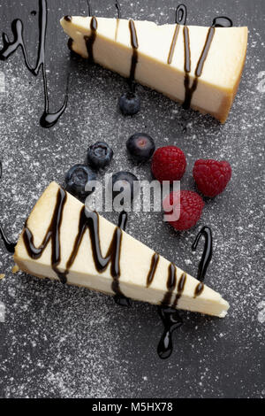 Two slices of cheesecake with liquorice sauce, blueberries, and raspberries on a slate board Stock Photo