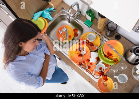High Angle View Of Stressed Young Woman Looking At Unwashed Utensils In Kitchen Stock Photo