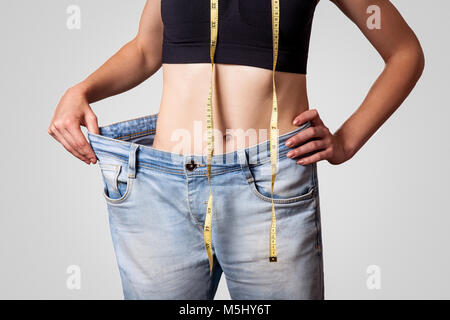 Close-up of slim waist of young woman in big jeans showing successful weight loss, isolated on light gray background, diet concept. Stock Photo