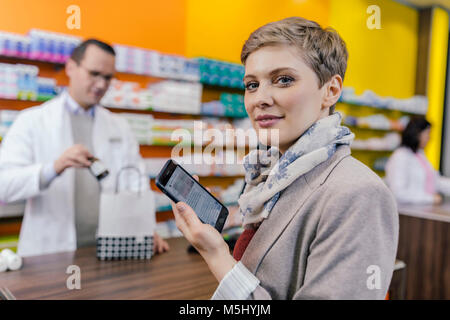 Portrait of woman with cell phone at counter in pharmacy Stock Photo