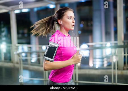 Young woman in pink sportshirt running in city at night Stock Photo