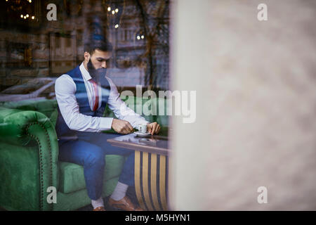 Fashionable young man sitting on couch in a cafe Stock Photo