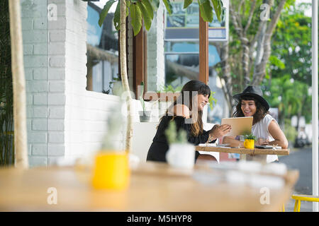 Two smiling women sharing tablet outside a cafe Stock Photo