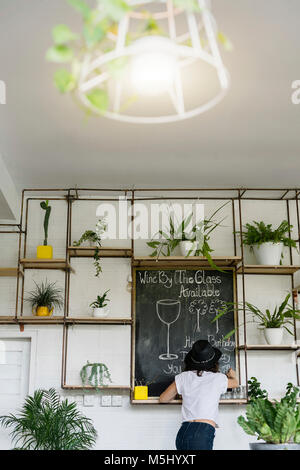Woman with black hat writing on chalkboard in a cafe Stock Photo