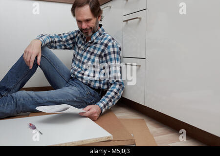 Man in casual clothes assembling the kitchen furniture Stock Photo