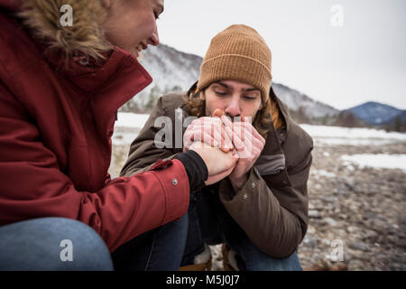 Couple on a trip in winter with man warming hands of woman
