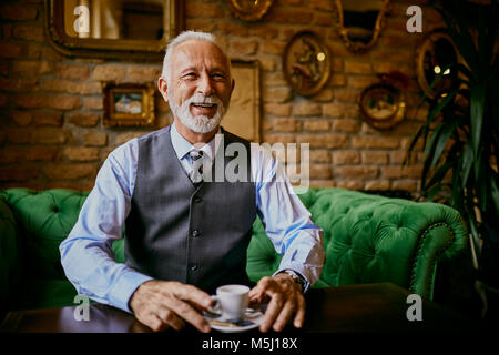 Portrait of elegant senior man sitting on couch in a cafe smiling Stock Photo