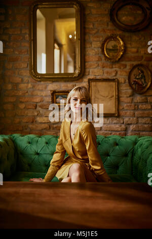 Portrait of beautiful seductive woman sitting on sofa against wall at ...