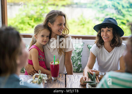Woman with girl on her lap smiling at her friend in cafe Stock Photo