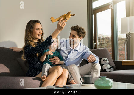 Happy parents and son playing with wooden toy plane on sofa at home Stock Photo