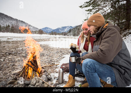 Couple on a trip in winter having a break at camp fire Stock Photo
