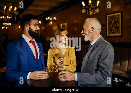 Two elegant men and woman socializing in a bar Stock Photo