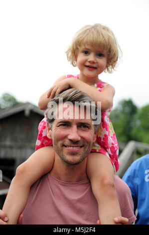 Portrait of happy man carrying his little daughter on shoulders