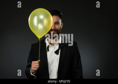Portrait of a young man holding a balloon, wearing loose black tie Stock Photo