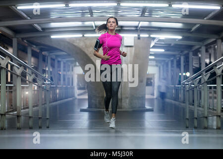 Young woman in pink sportshirt running in modern metro station at night Stock Photo