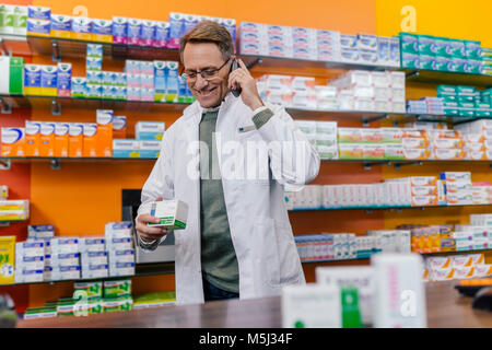 Smiling pharmacist talking on phone at counter in pharmacy Stock Photo