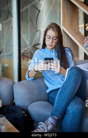 Young woman sitting in cafe using smartphone Stock Photo