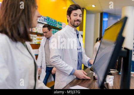 Portrait of smiling pharmacist with colleagues at counter in pharmacy Stock Photo