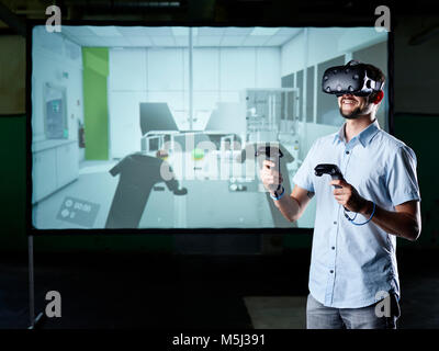 Smiling man wearing VR glasses in front of screen Stock Photo