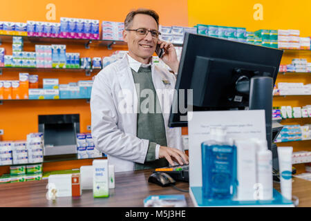 Smiling pharmacist talking on phone at counter in pharmacy Stock Photo